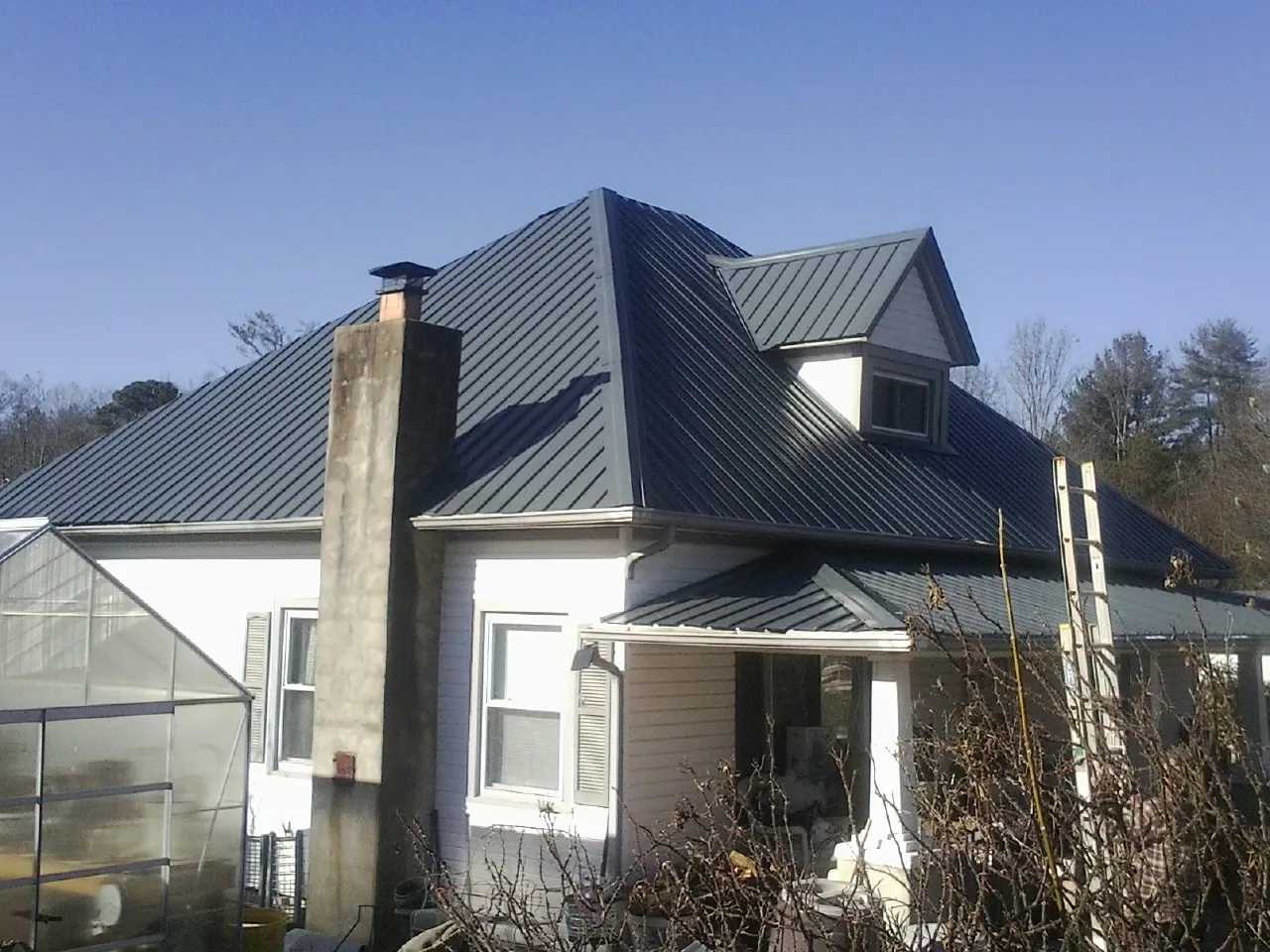 Dark blue standing seam metal roof on a white farmhouse with dormer — Slate & Tile Roof Repair by Roofing Brothers in Wilsall