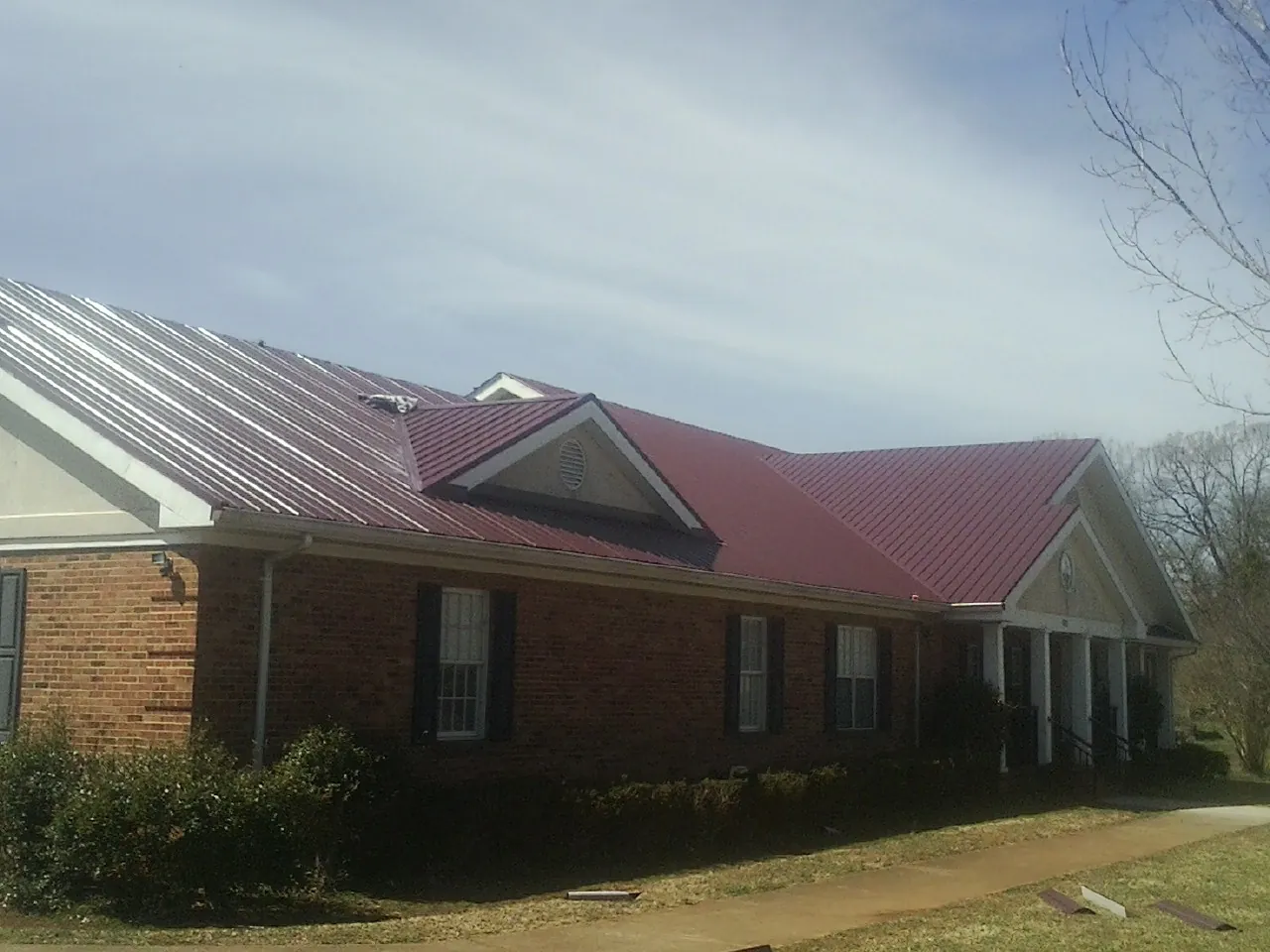 Red metal roof with gabled entries on a long brick building, from a Hail Damage Roof Repair job in Wilsall
