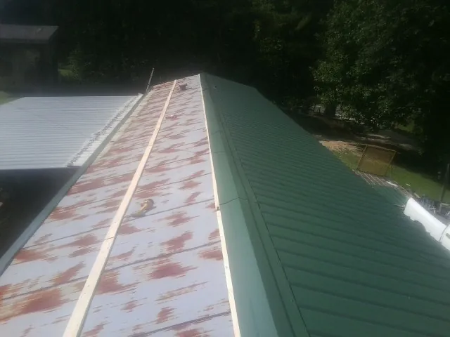 Old rusted panels beside newly installed green metal roofing — Wind Damage Roof Repair by Roofing Brothers in Wilsall